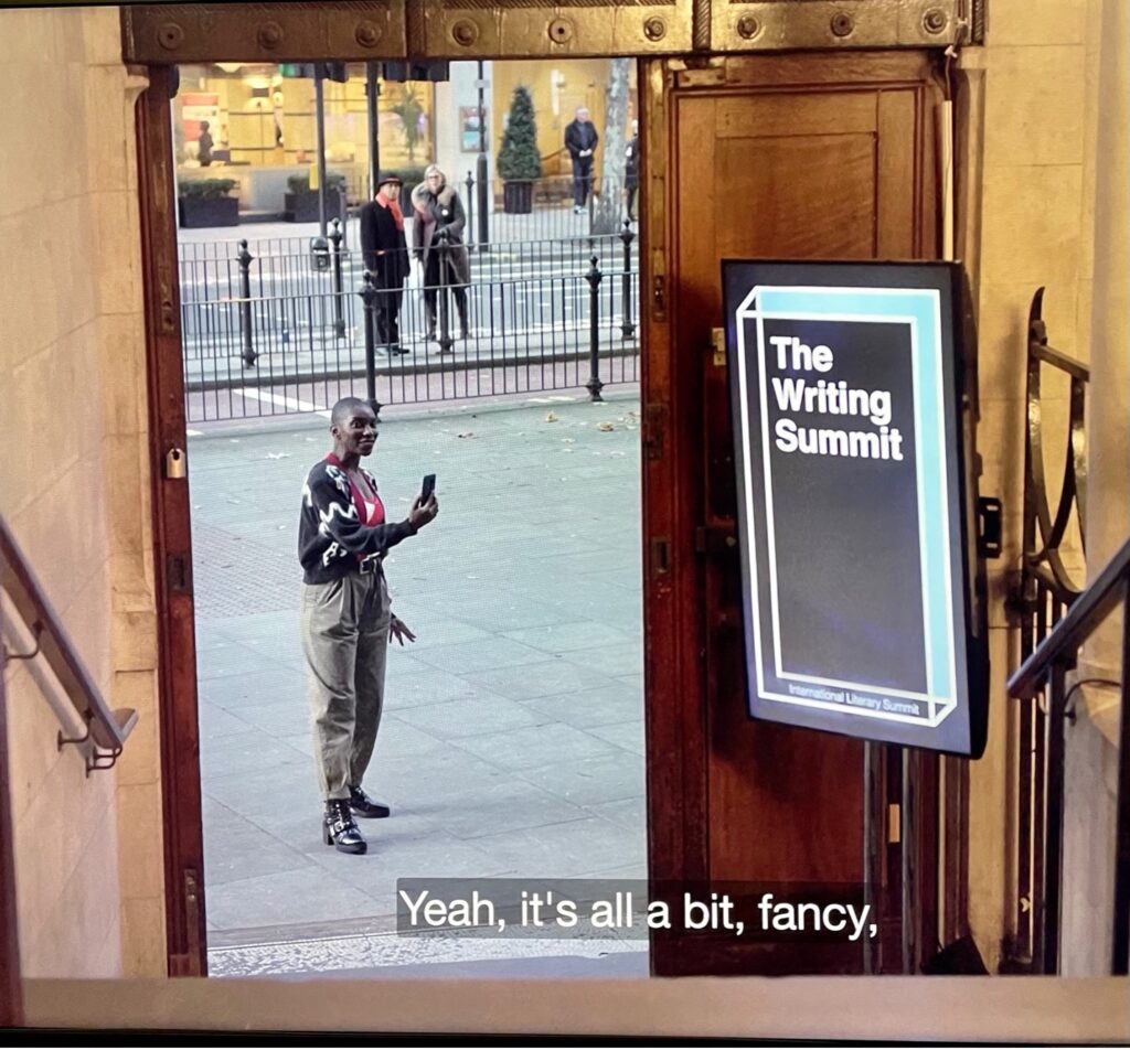 From a stone staircase a doorway is visible, with a young woman, Arabella, outside on a city street. An electronic display by the door reads