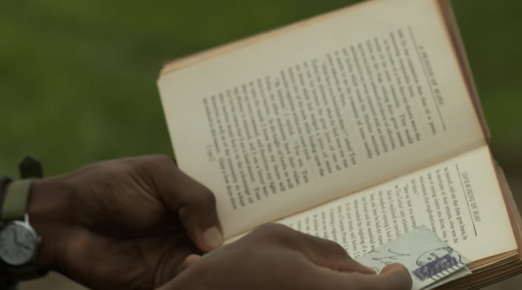A pair of hands hold a book open against a green background. The right hand also holds an envelope against the page.