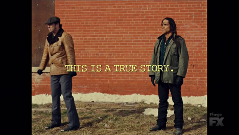 Two men standing in front of a brick wall, dressed for cold weather. Yellow text reads: