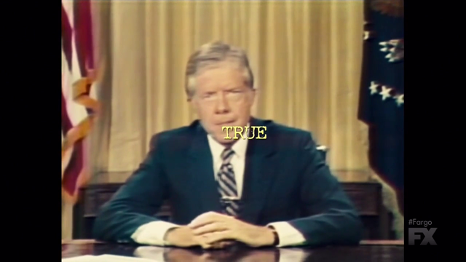Jimmy Carter sits at a desk in a blue suit. Flags and a yellow curtain are behind him. Yellow text superimposed on his face reads: