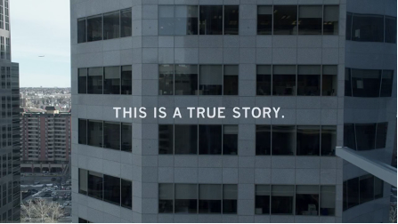 The exterior of a grey office building with large glass windows. Text reads: