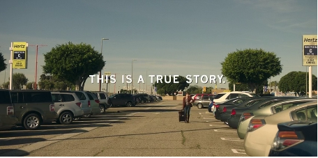 A woman wheeling a suitcase through a rental car parking lot. Text reads: