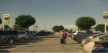 A woman wheeling a suitcase through a rental car parking lot. Only the word