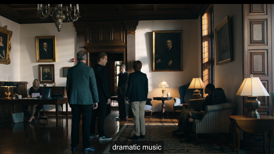 A small group of people in a large office. The office is dimly, warmly lit with a few short lamps and decorated with portraits of formally dressed individuals. The son, whose future is being decided, stands as his father and the headmaster converse.